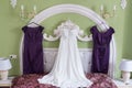 White wedding dress and two lilac bridesmaidÃ¢â¬â¢s dresses on a hanger on the wall. Morning of the bride. Fees.